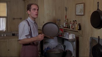 Movie still from “Places in the Heart” (1984), directed by Robert Benton – A man holding a frying pan in a kitchen; Medium shot, Low angle