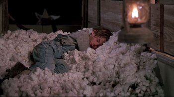Movie still from “Places in the Heart” (1984), directed by Robert Benton – A young boy laying in a pile of cotton stuffing; Medium shot, High angle