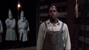 Movie still from “Places in the Heart” (1984), directed by Robert Benton – A man in overalls standing next to a person in a white robe; Medium shot, Over the shoulder angle