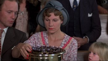 Movie still from “Places in the Heart” (1984), directed by Robert Benton – A woman in a hat and a dress looking at a jar; Close Up shot, Low angle