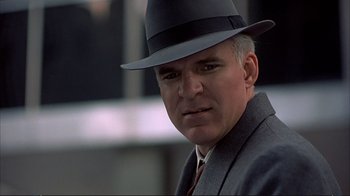 Movie still from “Planes, Trains & Automobiles” (1987), directed by John Hughes – A person wearing a suit and a hat; Close Up shot, Over the shoulder angle