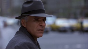 Movie still from “Planes, Trains & Automobiles” (1987), directed by John Hughes – An older man wearing a gray hat and a gray coat; Close Up shot, Over the shoulder angle