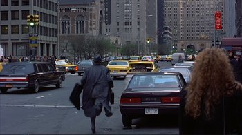 Movie still from “Planes, Trains & Automobiles” (1987), directed by John Hughes – A man in a raincoat walking down a street; Wide shot, Over the shoulder angle