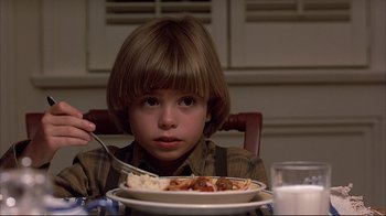 Movie still from “Planes, Trains & Automobiles” (1987), directed by John Hughes – A boy sitting at a dinner table with a plate of food in front of him; Close Up shot, High angle