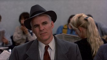 Movie still from “Planes, Trains & Automobiles” (1987), directed by John Hughes – A man wearing a suit and a hat; Close Up shot, Over the shoulder angle