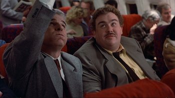 Movie still from “Planes, Trains & Automobiles” (1987), directed by John Hughes – A couple of men sitting next to each other on a couch; Medium shot, Low angle