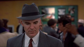 Movie still from “Planes, Trains & Automobiles” (1987), directed by John Hughes – A man in a suit and a hat is standing in a crowd of people; Close Up shot, Over the shoulder angle