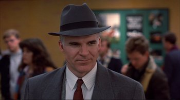 Movie still from “Planes, Trains & Automobiles” (1987), directed by John Hughes – A man wearing a hat and a suit and tie; Close Up shot, Over the shoulder angle