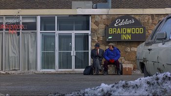 Movie still from “Planes, Trains & Automobiles” (1987), directed by John Hughes – Two people sitting on a bench outside of a hotel; Wide shot, Low angle