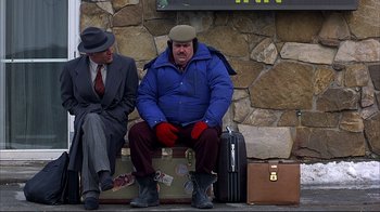 Movie still from “Planes, Trains & Automobiles” (1987), directed by John Hughes – A man sitting on top of a suitcase next to another man; Wide shot, High angle