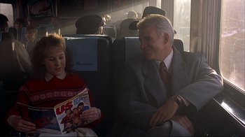 Movie still from “Planes, Trains & Automobiles” (1987), directed by John Hughes – A man sitting next to a woman on a train; Medium shot, Over the shoulder angle
