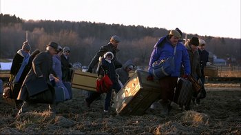 Movie still from “Planes, Trains & Automobiles” (1987), directed by John Hughes – A group of people walking across a dirt field carrying suitcases; Wide shot, High angle
