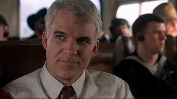 Movie still from “Planes, Trains & Automobiles” (1987), directed by John Hughes – A person wearing a suit and tie; Close Up shot, Over the shoulder angle
