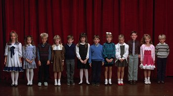 Movie still from “Planes, Trains & Automobiles” (1987), directed by John Hughes – A group of children standing in front of a red curtain; Wide shot, Overhead angle