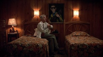 Movie still from “Planes, Trains & Automobiles” (1987), directed by John Hughes – An older man sitting on a chair in a room; Wide shot, Low angle