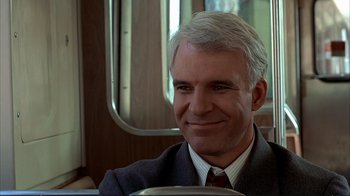 Movie still from “Planes, Trains & Automobiles” (1987), directed by John Hughes – A man in a suit and tie sitting on a bus; Close Up shot, Over the shoulder angle