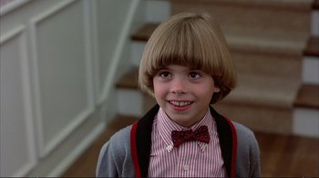 Movie still from “Planes, Trains & Automobiles” (1987), directed by John Hughes – A young boy with a bow tie in a room with stairs; Close Up shot, High angle