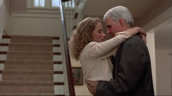 Movie still from “Planes, Trains & Automobiles” (1987), directed by John Hughes – An older man and a young woman hugging in front of a staircase; Medium shot, Low angle