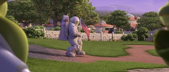 Movie still from “Planet 51” (2009), directed by Javier Abad – An animated figure holding an american flag on a sidewalk; Wide shot, High angle