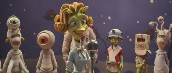 Movie still from “Planet 51” (2009), directed by Javier Abad – A group of people standing next to each other with a microphone; Medium shot, Over the shoulder angle