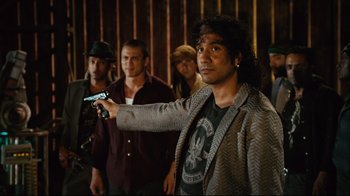 Movie still from “Planet Terror” (2007), directed by Robert Rodriguez – A man holding a gun in front of a group of men; Medium shot, Over the shoulder angle
