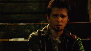 Movie still from “Planet Terror” (2007), directed by Robert Rodriguez – A man sitting on a wooden bench smoking a cigarette; Close Up shot, Low angle