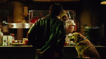 Movie still from “Planet Terror” (2007), directed by Robert Rodriguez – A man standing next to a dog in front of a counter; Medium shot, Over the shoulder angle