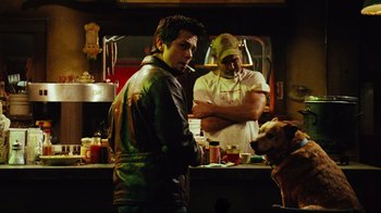 Movie still from “Planet Terror” (2007), directed by Robert Rodriguez – A man standing next to a dog in front of a counter; Medium shot, Over the shoulder angle