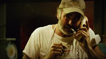 Movie still from “Planet Terror” (2007), directed by Robert Rodriguez – A man with a hat smoking while talking on the phone; Close Up shot, Low angle