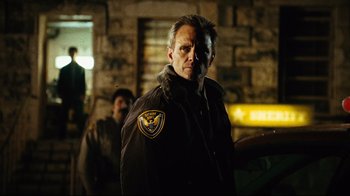 Movie still from “Planet Terror” (2007), directed by Robert Rodriguez – A man in a brown jacket standing in front of a brick wall; Close Up shot, Over the shoulder angle