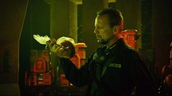 Movie still from “Planet Terror” (2007), directed by Robert Rodriguez – A man in a black jacket holding a white object in his hand; Close Up shot, Low angle