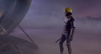 Movie still from “Planet of the Vampires” (1965), directed by Mario Bava – A man in a spacesuit and helmet standing next to an object in the fog; Wide shot, Low angle