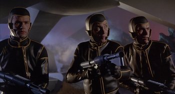 Movie still from “Planet of the Vampires” (1965), directed by Mario Bava – A group of men in black and yellow suits holding a gun; Medium shot, Low angle