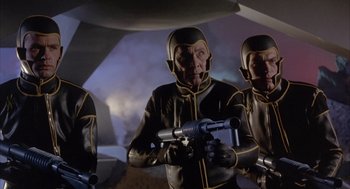 Movie still from “Planet of the Vampires” (1965), directed by Mario Bava – A group of people in black and yellow suits holding guns; Medium shot, Low angle