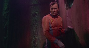 Movie still from “Planet of the Vampires” (1965), directed by Mario Bava – A man in a red and blue suit standing next to a wall; Medium shot, Low angle