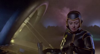 Movie still from “Planet of the Vampires” (1965), directed by Mario Bava – A woman in a black and yellow costume holding a red object; Medium shot, Low angle