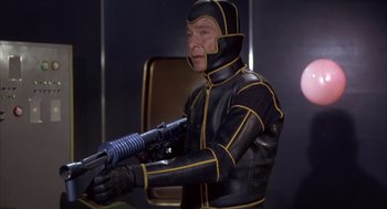 Movie still from “Planet of the Vampires” (1965), directed by Mario Bava – A man in a black and yellow suit holding a gun; Medium shot, High angle