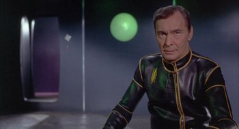 Movie still from “Planet of the Vampires” (1965), directed by Mario Bava – A man in a green and black suit standing in front of a green ball; Medium shot, Low angle