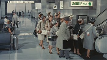 Movie still from “Playtime” (1967), directed by Jacques Tati – A group of people standing in line at a train station; Wide shot, High angle