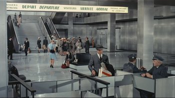 Movie still from “Playtime” (1967), directed by Jacques Tati – A group of people waiting at an airport terminal; Wide shot, High angle