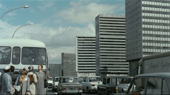 Movie still from “Playtime” (1967), directed by Jacques Tati – A woman standing on the side of a road next to cars; Extreme Wide shot, Low angle