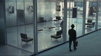 Movie still from “Playtime” (1967), directed by Jacques Tati – A man standing in front of a window in a room; Wide shot, High angle