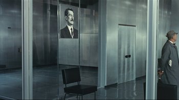Movie still from “Playtime” (1967), directed by Jacques Tati – A chair in front of a picture of a man in a suit; Wide shot, Low angle