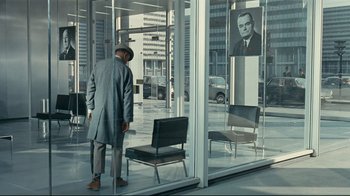 Movie still from “Playtime” (1967), directed by Jacques Tati – A man standing in front of a glass window; Wide shot, Over the shoulder angle