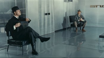 Movie still from “Playtime” (1967), directed by Jacques Tati – Two men sitting on chairs in a room; Wide shot, Over the shoulder angle