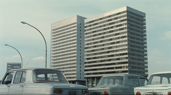 Movie still from “Playtime” (1967), directed by Jacques Tati – Cars are parked in front of a tall building; Extreme Wide shot, Low angle