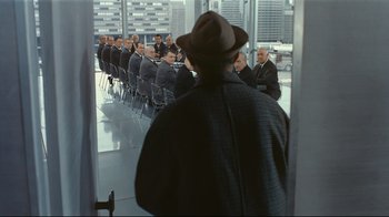 Movie still from “Playtime” (1967), directed by Jacques Tati – A group of men in suits sitting in front of a window; Wide shot, Over the shoulder angle