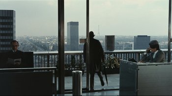 Movie still from “Playtime” (1967), directed by Jacques Tati – A man walking on a balcony with a view of a city; Wide shot, Over the shoulder angle