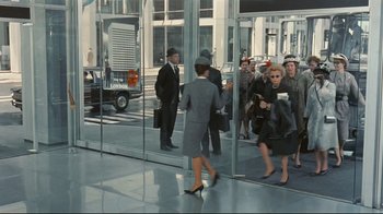Movie still from “Playtime” (1967), directed by Jacques Tati – A group of people standing in front of a glass building; Wide shot, Over the shoulder angle