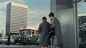 Movie still from “Playtime” (1967), directed by Jacques Tati – Two women are waiting to board a city bus; Wide shot, Low angle